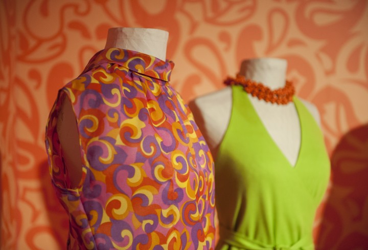Bunte Damenoutfits an Figurinen vor buntem Hintergrund in einer Ausstellung
