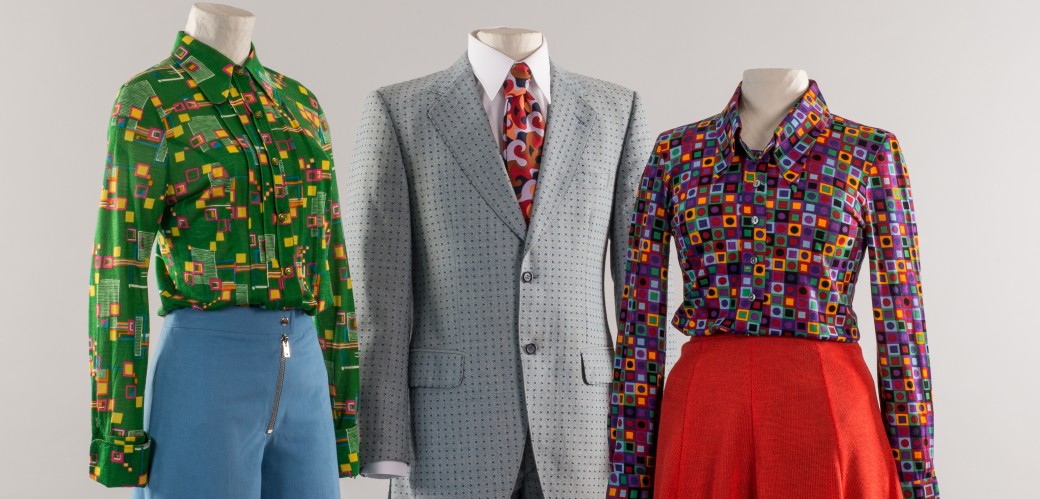 Drei Figurinen in Kleidung der 60er Jahre. Die Linke trägt eine bunte Bluse zu blauer Schlaghose. Die Mittlere einen Anzug mit bunter Krawatte. Die Rechte eine bunte Bluse zu einem roten Minirock.
