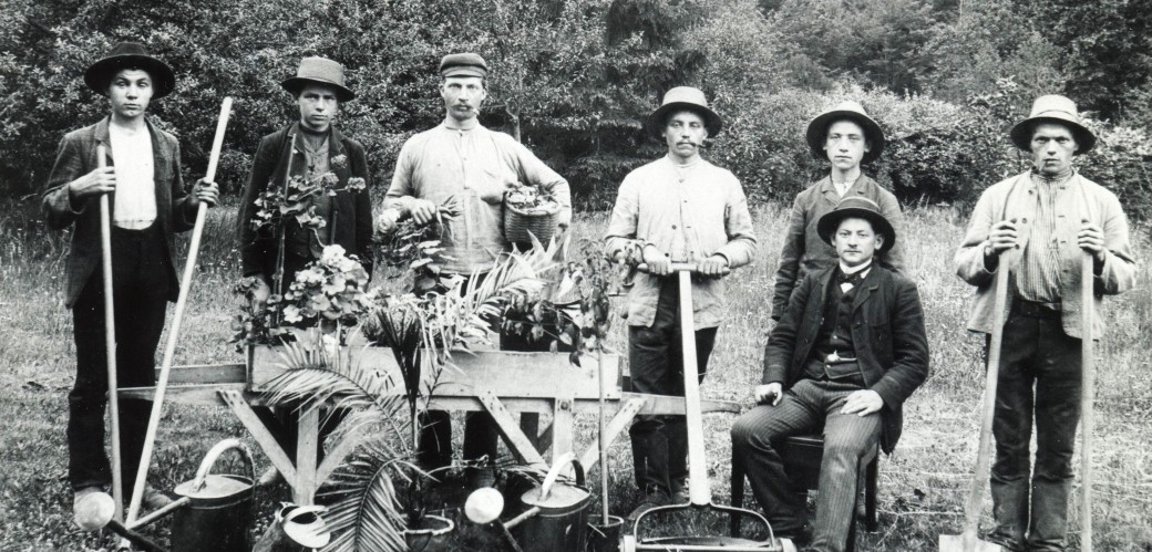 Historisches Schwarzweißfoto einer Gruppe Gärtner mit Arbeitsgeräten auf einer Wiese