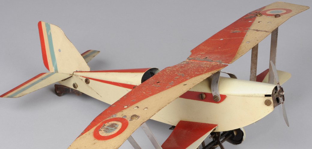 Modellflugzeug aus Metall in Cremeweiß und Rot vor grauem Grund.