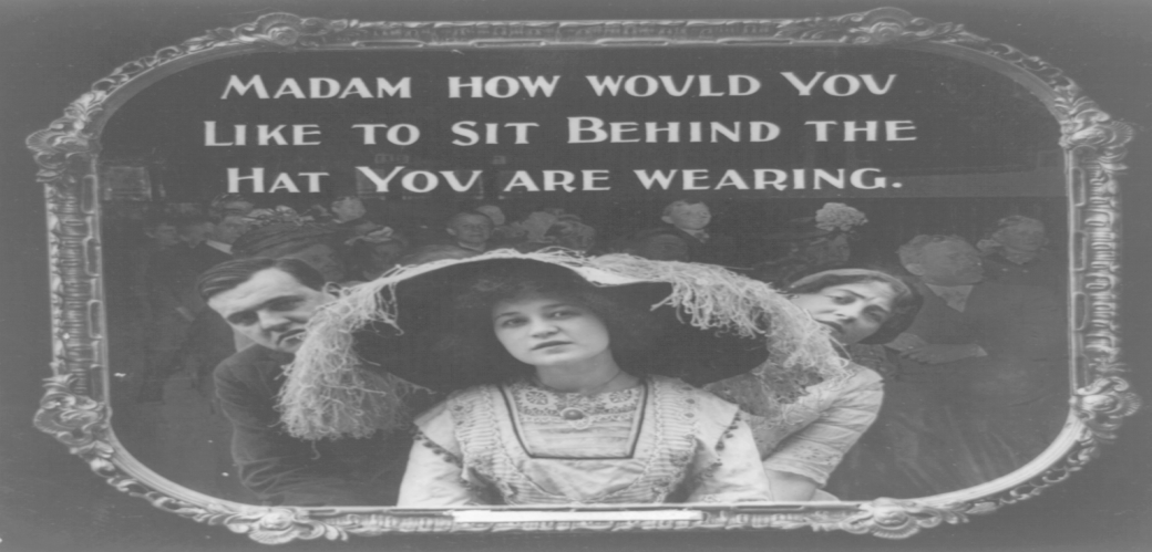 Schwarzweiß Bild einer Dame mit großem Hut im Kino. Hinter ihr versuchen zwei Leute an ihrem Hut vorbeizuschauen. 