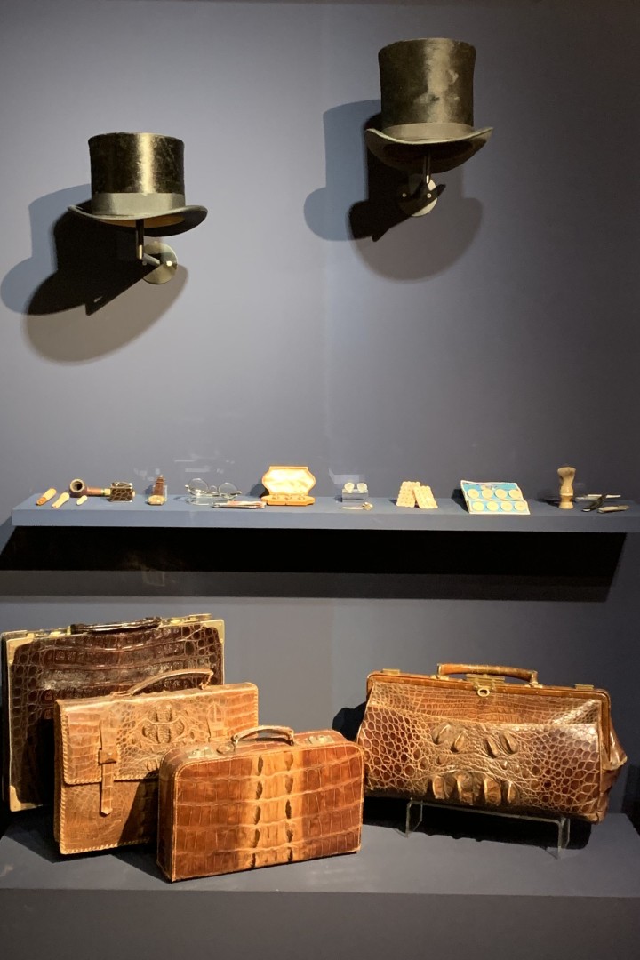 3 Taschen aus Leder und 2 Hüte auf Wandhalterungen in der Ausstellung