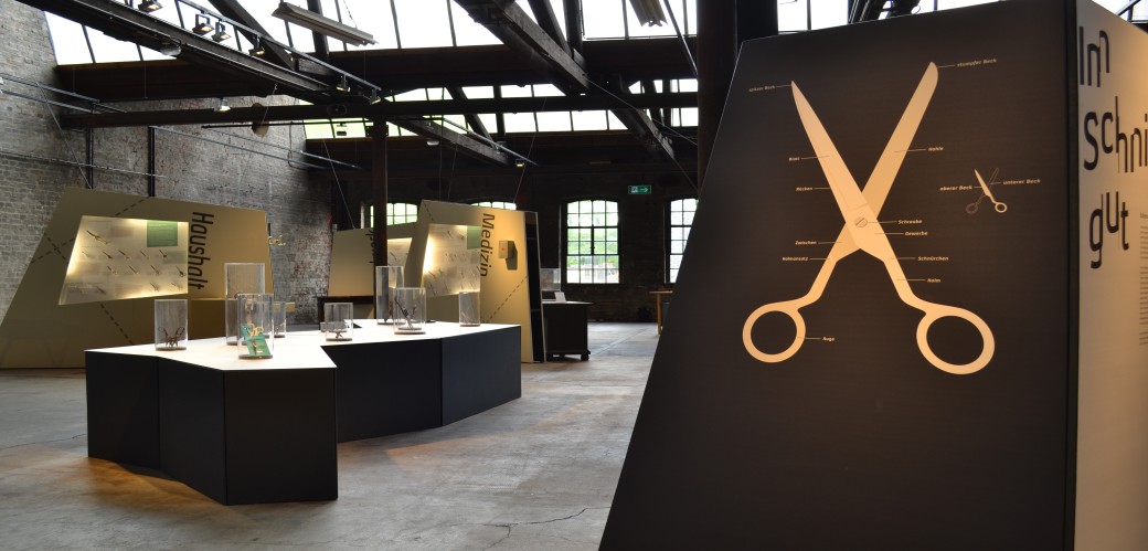 Ausstellungsraum mit Vitrinen und einer Scherengrafik an der Wand