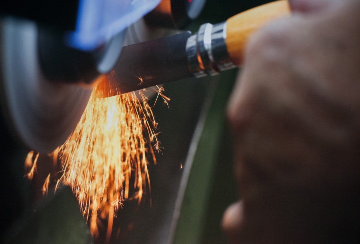 Detailansicht einer Hand, die ein Messer an einer Maschine unter Funkenflug schleift