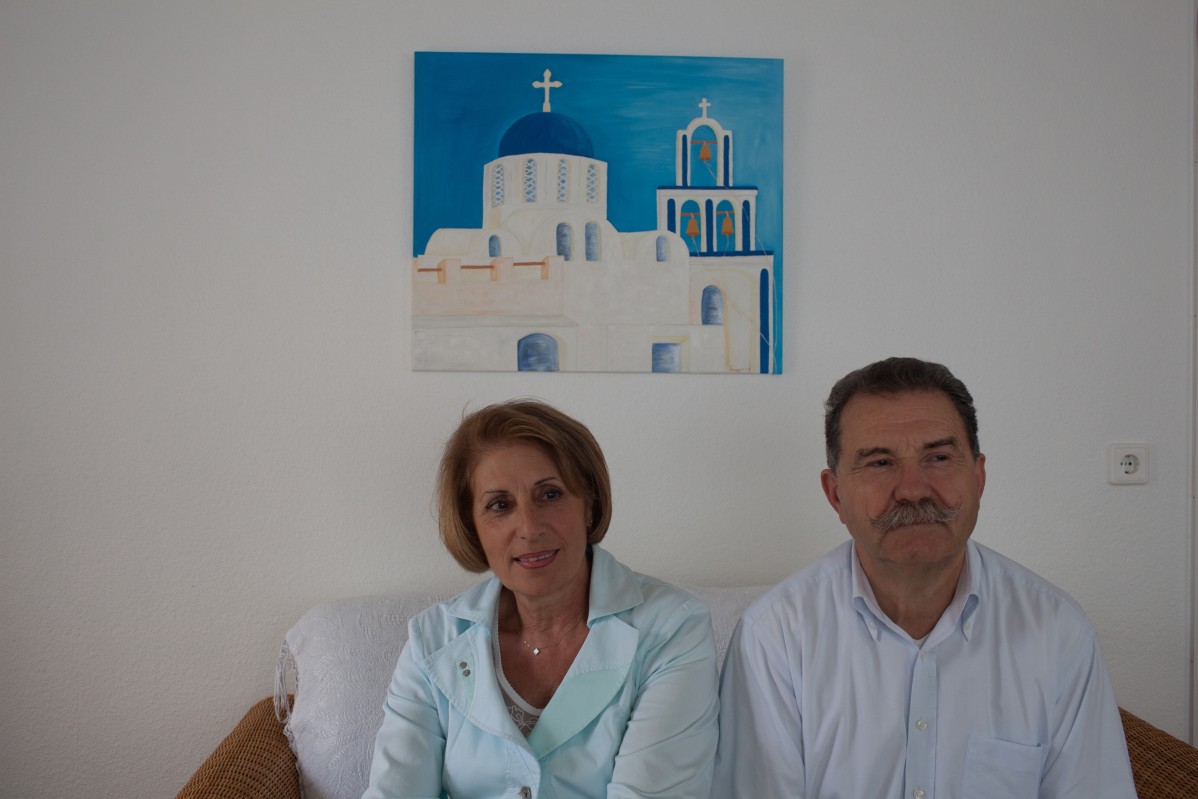Mann und Frau sitzen auf einem Sofa in ihrer Wohnung vor einem typischen Gemälde aus Griechenland.