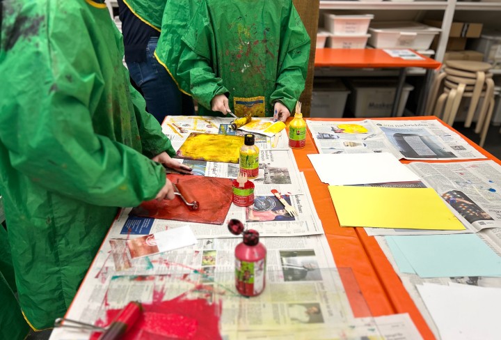 Foto von einem Tisch, auf dem Zeitungspapier ausgelegt ist. Kinder malen auf diesem Tisch Bilder.