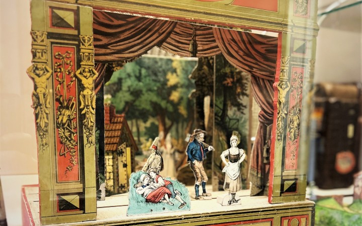 Miniaturbühne mit bemalten Figuren in historischen Kostümen vor einer Kulisse aus Bäumen und Häusern.
