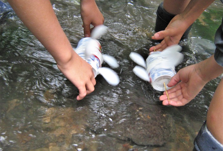 Foto von selbstgebastelten Wasserrädern, die in einen Fluss gehalten werden. Die Wasserräder wurden aus Joghurt Bechern gebastelt.