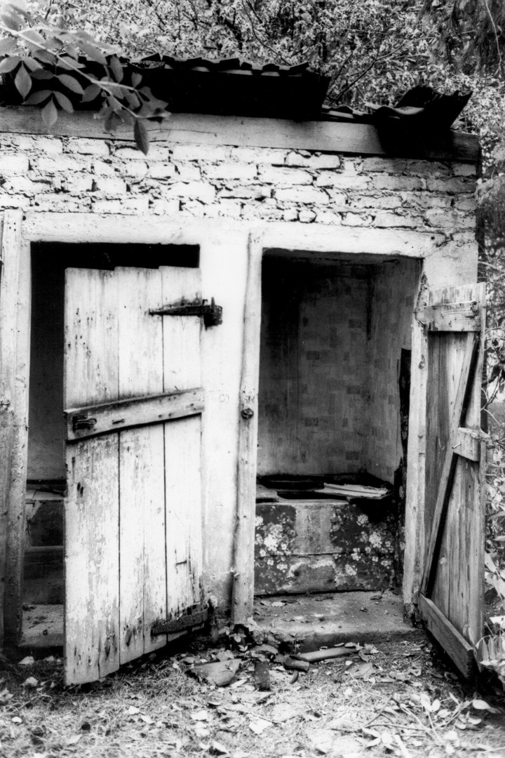 Schwarz/Weiß Foto zeigt ein gemauertes Plumpsklo mit zwei Holztüren die offen stehen