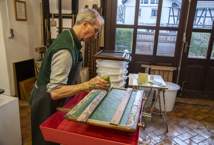 John Gerard bei der Gestaltung eines frisch geschöpften Papierbogens mit der Technik des sogenannten „Pulp Paintings“ oder auf Deutsch „Papierguss