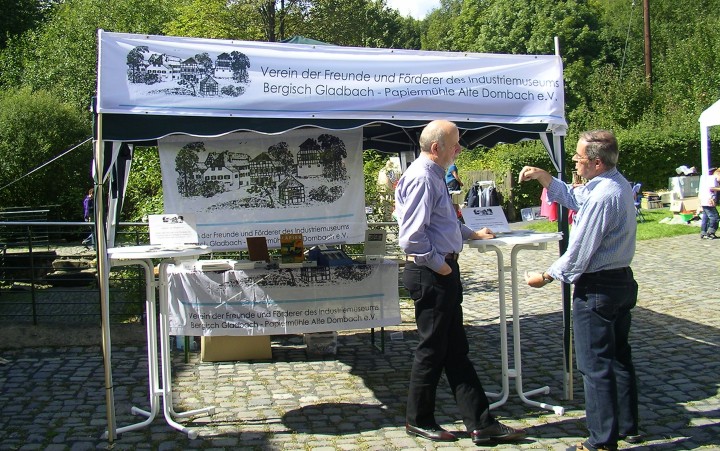 Two men are talking at a high table in front of an information stand