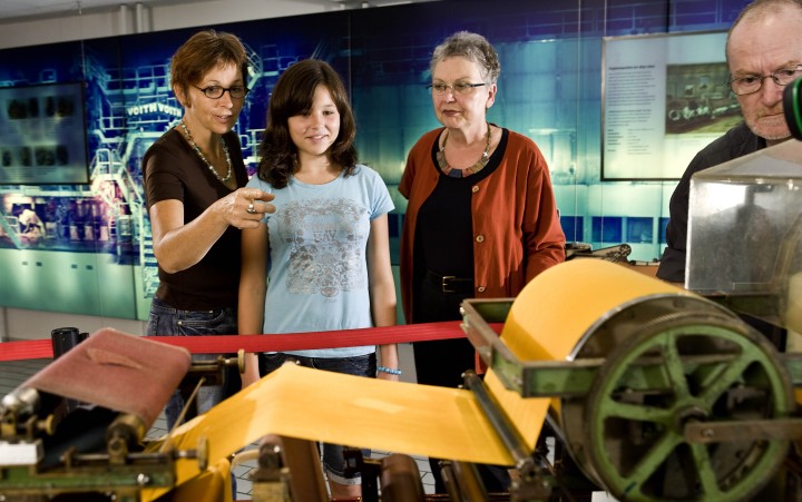 Drei Damen schauen eine große Papiermaschine an