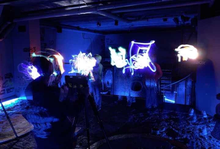 Foto von einem Keller, in welchem Leute stehen, die ein Graffiti mit Lightpainting machen.