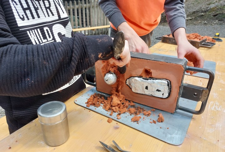 Kinder, die Sand von ihrem Metallguss abkratzen.
