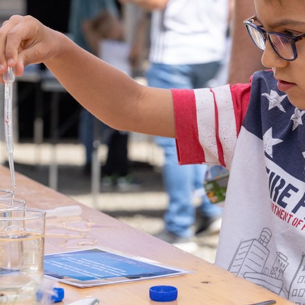 Junge, der mit einer Pipette Wasser in ein Glas macht.