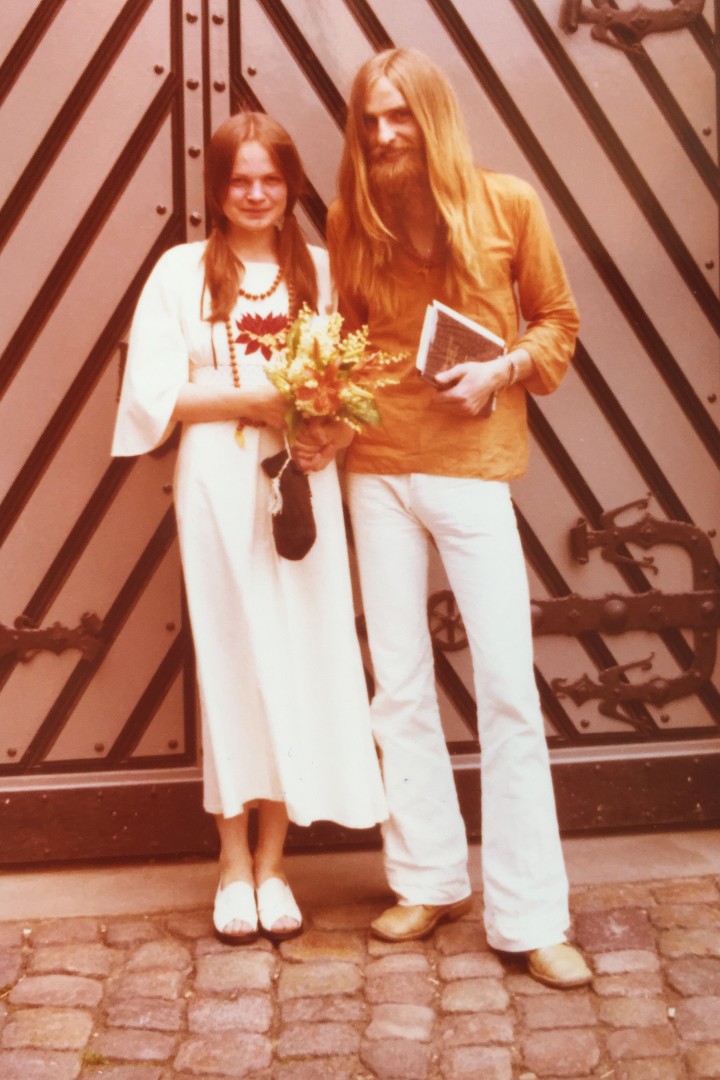 Foto zeigt eine Frau im weißen Kleid und ein Mann in weißer Hose und oragenem Hemd als Paar