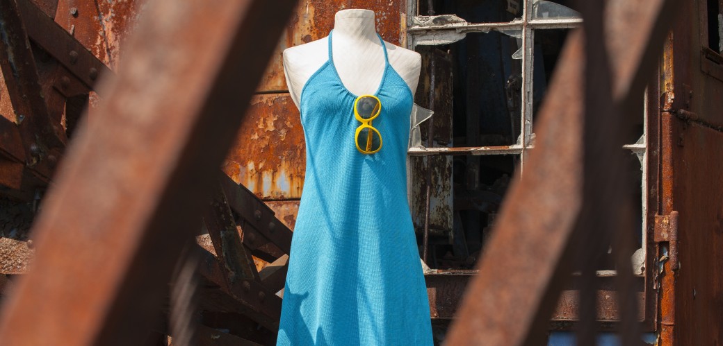 Figurine mit einem hellblauen Neckholder-Kleid. Im Ausschnitt des Kleides ist eine runde, gelbe Sonnenbrille eingehängt.