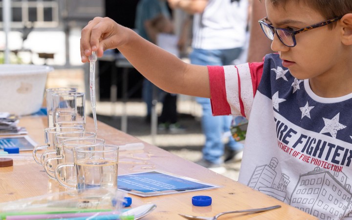 Kleiner Junge, welcher mit einer Pipette Wasser in Gläser umfüllt