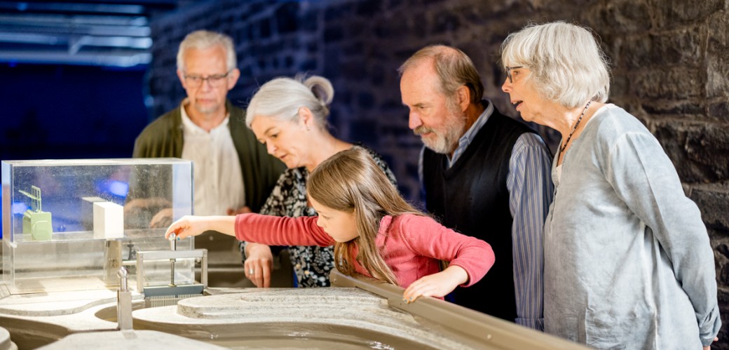 Eine Gruppe von älteren Personen und einem Kind experimentieren am Wasserkraftmodell.