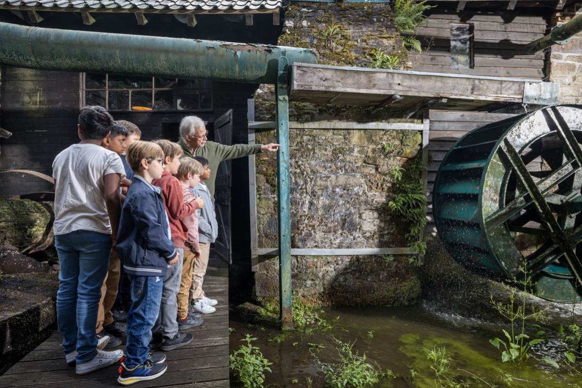 Group of children looks at the working waterwheel.