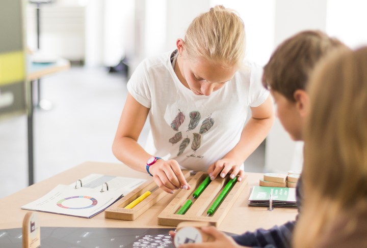 Drei Kinder stehen um einen Tisch herum, auf dem eine skizzierte Landkarte abgebildet ist. Sie haben Bausteine mit verschiedenen Energielieferanten zur Hand, die Sie beliebig einsetzen und platzieren können.