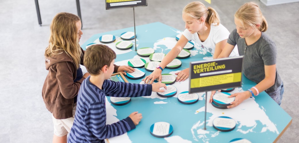 Vier Kinder stehen um einen Tisch herum und spielen zusammen das Quartett der erneuerbaren Energien