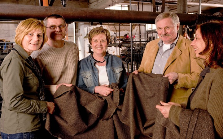 Two men and three women are fiddling with a brown blanket