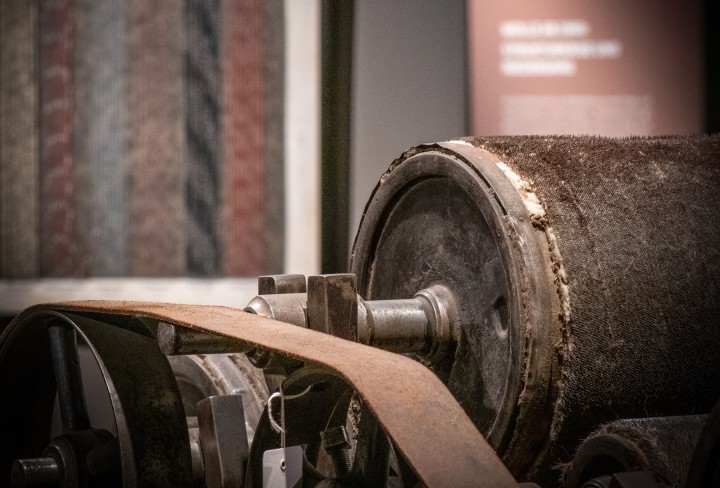 Nahaufnahme einer alten, abgenutzten Walzenmaschine in einem Museum mit unscharfem Gemälde im Hintergrund.