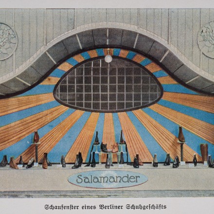 Schaufenster Berliner Schuhgeschäfts. Man sieht Schuhe der Marke "Salamander". Das Schaufenster zeigt eine halbkreisförmige Gestaltung mit blauen und goldenen Strahlen, mehrere Schuhmodelle und den Schriftzug "Salamander".