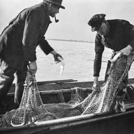 Historisches schwarz-weiß Foto von zwei Fischern, die Fischernetze festhalten, in einem Fischerboot.