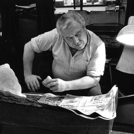 Historische Fotografie von Mann der über Zeitung gebeugt sitzt und ein Pausenbrot in der Hand hält