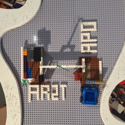 Foto von Legosteinen, die einmal eine Arztpraxis darstellen und einmal eine Apotheke. Die beiden Gebäude stehen nah beieinander und werden durch einen Legostein verbunden. Daneben steht ein Auto aus Lego. 
