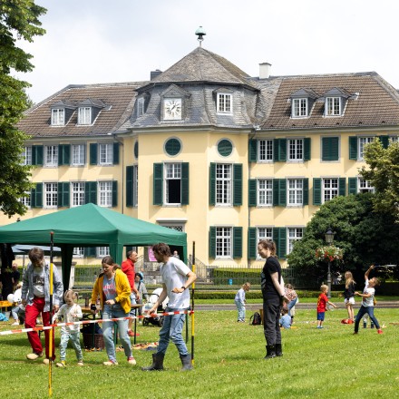 Das Foto zeigt das Herrenhaus der Textilfabrik Cromford. Im Vordergrund sind Pavillons aufgebaut und Familien spielen auf der Wiese.