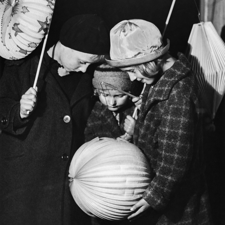 Drei Kinder mit Laternen in den Händen, die das Licht andächtig betrachten.