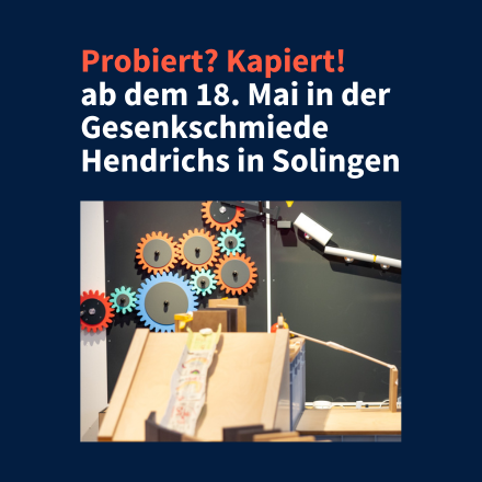 Foto eines Ausstellungsraums mit dem Text "Probiert? Kapiert! ab dem 18. Mai in der Gesenkschmiede Hendrichs in Solingen"