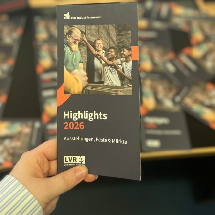 Der Eventkalender 2026 vom LVR-Industriemuseum wird mit einer Hand gehalten. Im Hintergrund sieht man unscharf weitere Eventkalender.