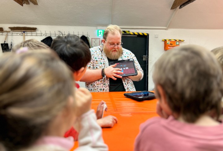 Ein Mann führt einen Tabletcomputer mit einer Musikbearbeitungs-Software einer Gruppe von Kindern vor.