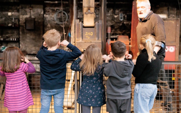 Eine Gruppe Kinder steht vor einem Fallhammer und hält sich die Ohren zu.