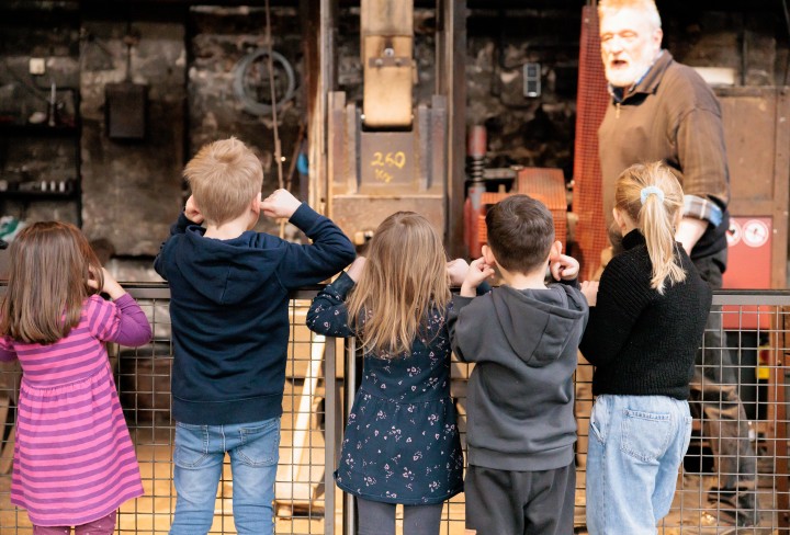 Eine Gruppe Kinder steht vor einem Fallhammer und hält sich die Ohren zu.