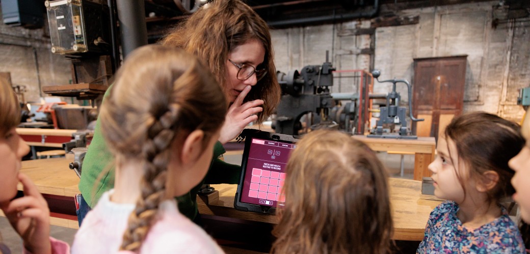 Eine Frau denonstriert vor einer Gruppe von Kindern einen Tabletcomputer.