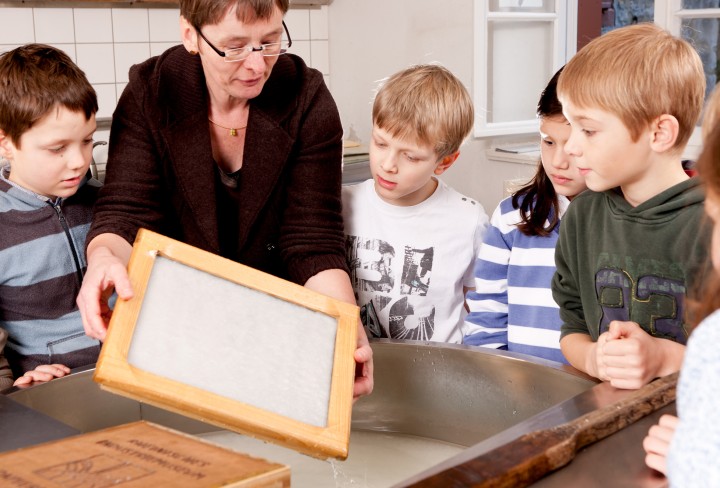 Kinder mit Museumspädagogin beim Papierschöpfen an der Bütte