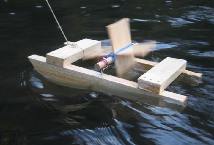 Ein selbstgebautes Spielzeug-Boot aus Holz auf einem Bach schwimmend.