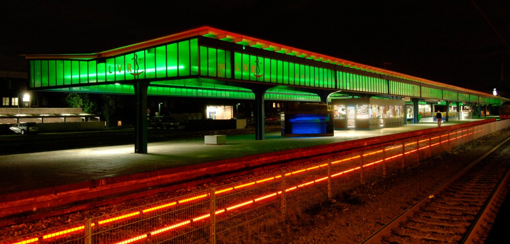 Ein Bahnsteig in der Nacht, der grün und rot beleuchtet wird.