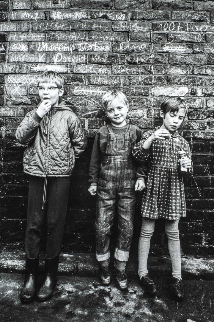 Schwarz-Weiß Foto zeigt drei Kinder die vor einer Mauer stehen