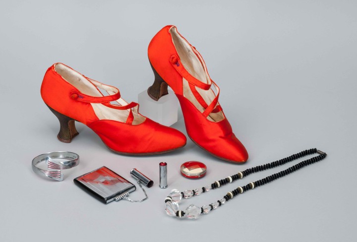 Foto zeigt rote Schuhe, Kette, Schmicketui und eine Puderdose