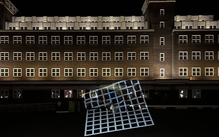 Großes, beleuchtetes Industriegbäude bei Nacht, davor eine Lichtinstallation