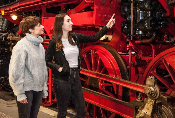 Two young ladies look at a red and black steam locomotive in the museum