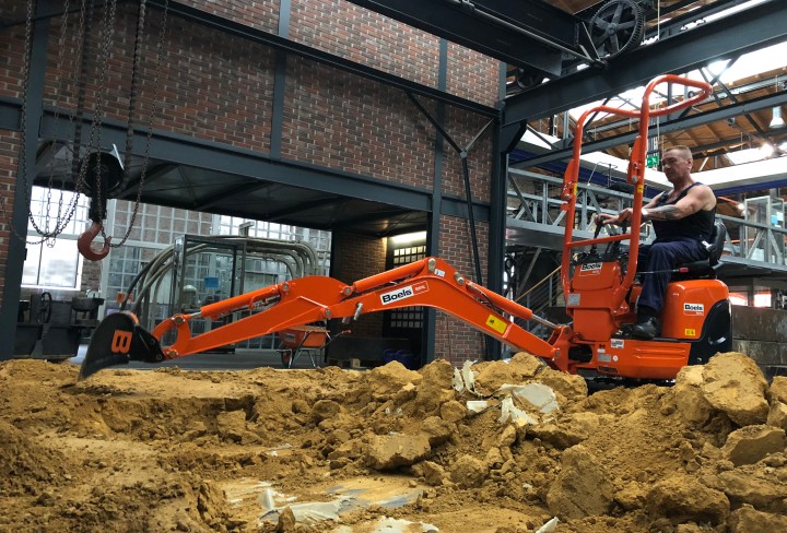 Man in the excavator clears sand from a large hall