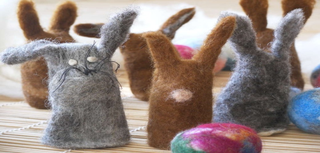 Mehrere aus Filz gefertigte Osterhasenfiguren in Braun- und Grautönen mit bunten Ostereiern auf einer hellen Unterlage