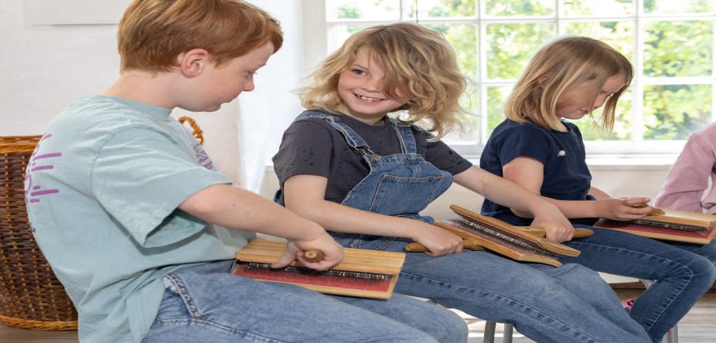 Drei Kinder sitzen nebeneinander und halten jeweils eine Holztafel mit Drahtborsten in den Händen.
